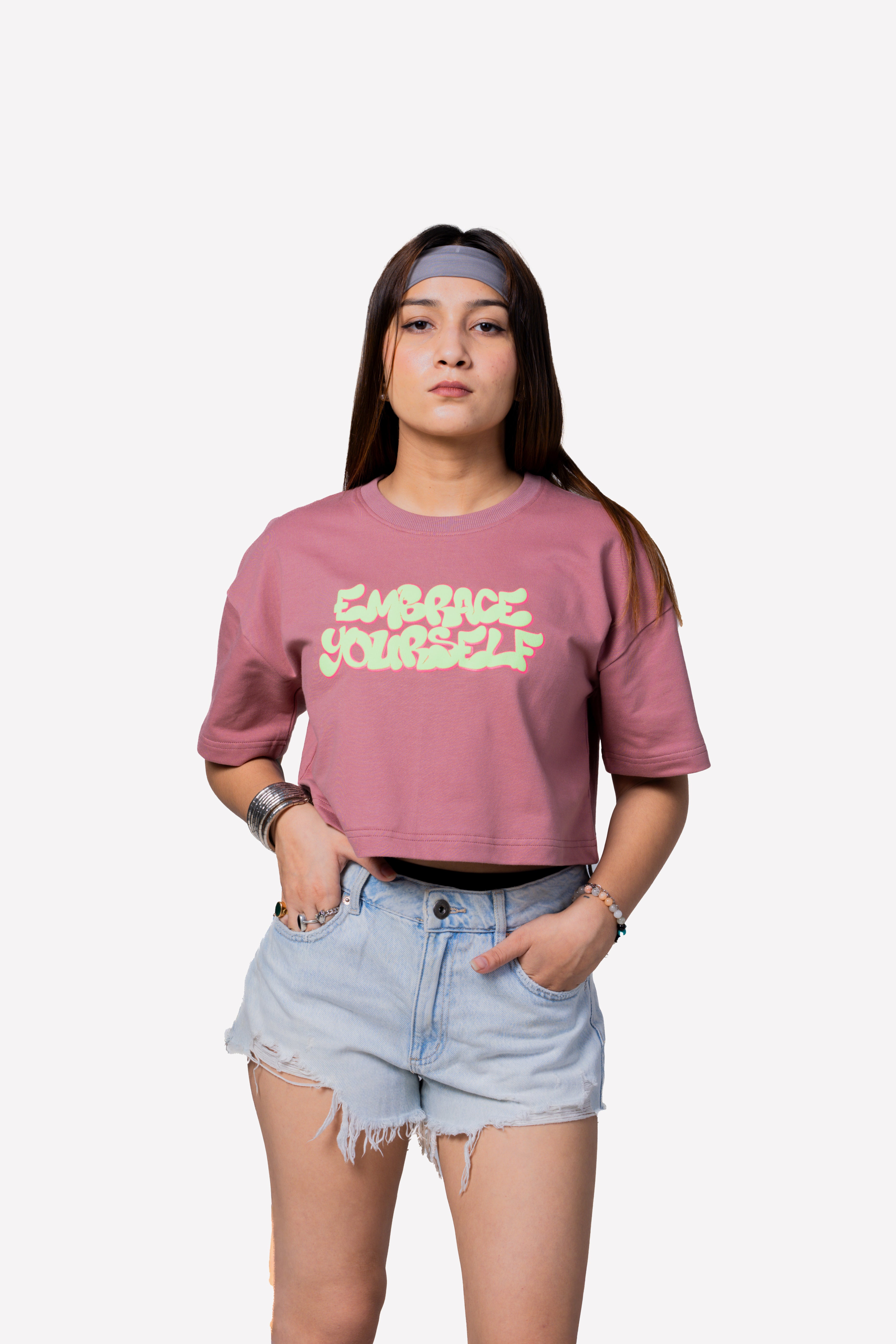 Person wearing a pink t-shirt with text and denim shorts on a white background