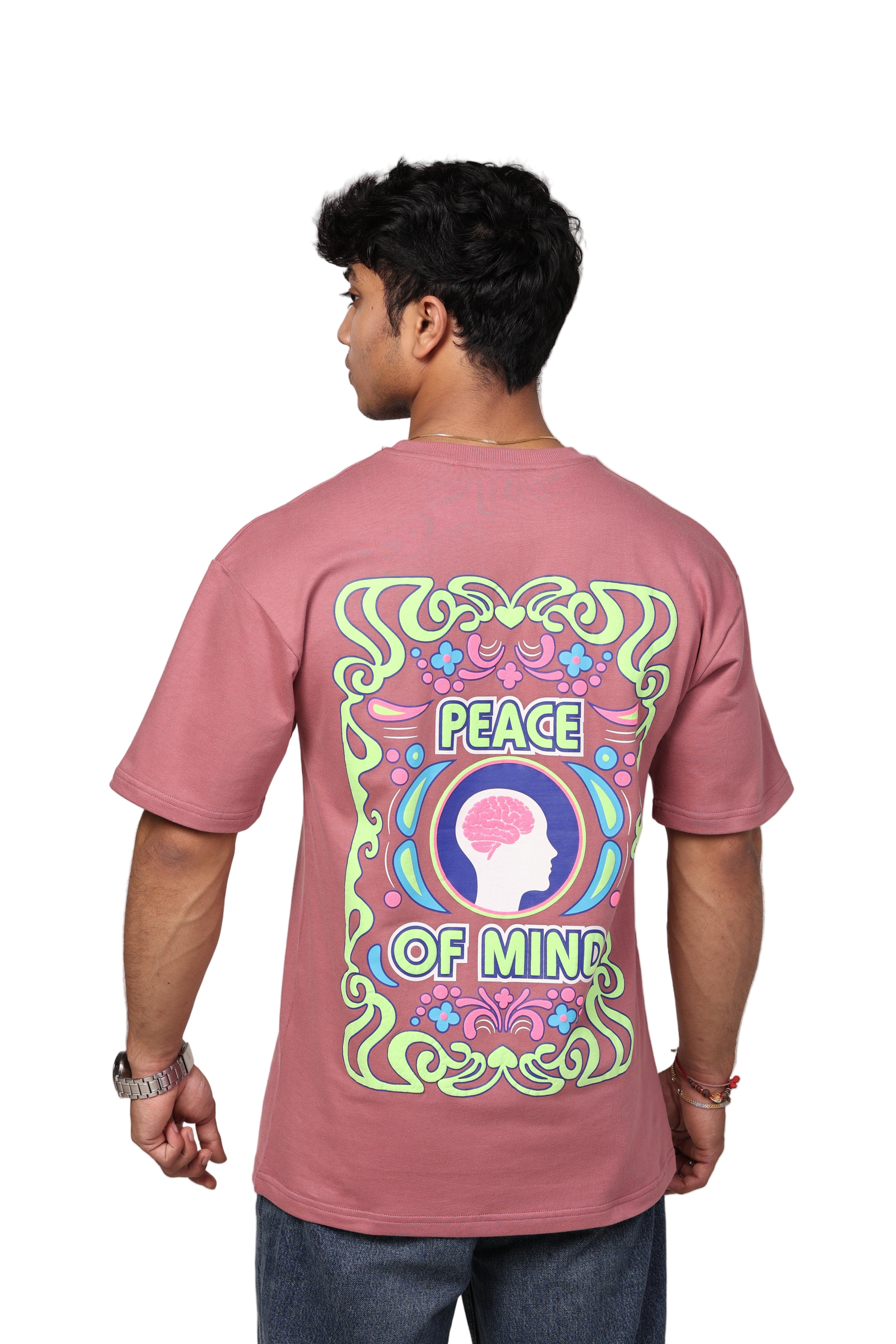 Person wearing a pink t-shirt with a colorful design and text on the back against a beige background