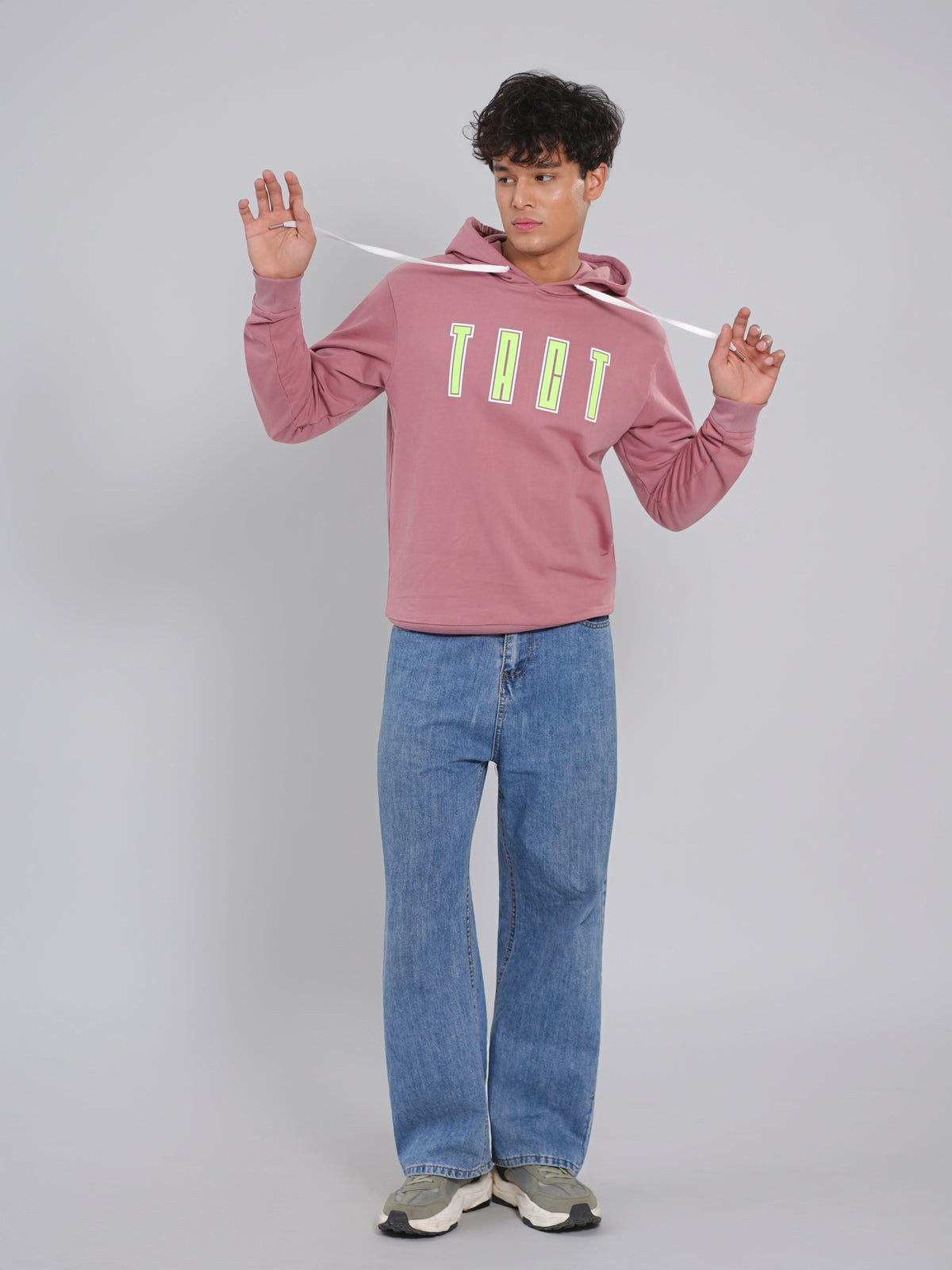 Person wearing a pink hoodie with 'TACT' text and blue jeans on a gray background